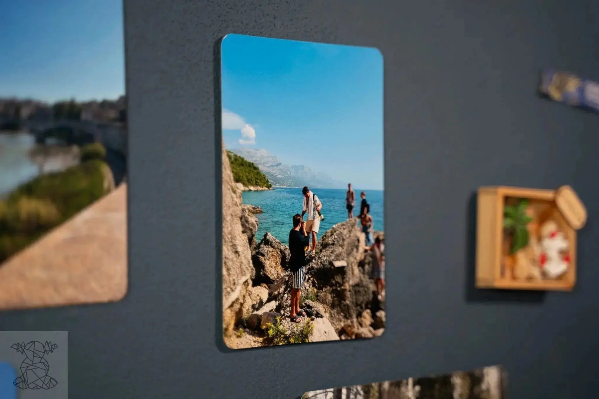 Close-up small glossy metal print of coastal hikers on blue gallery wall, capturing crisp outdoor detail.
