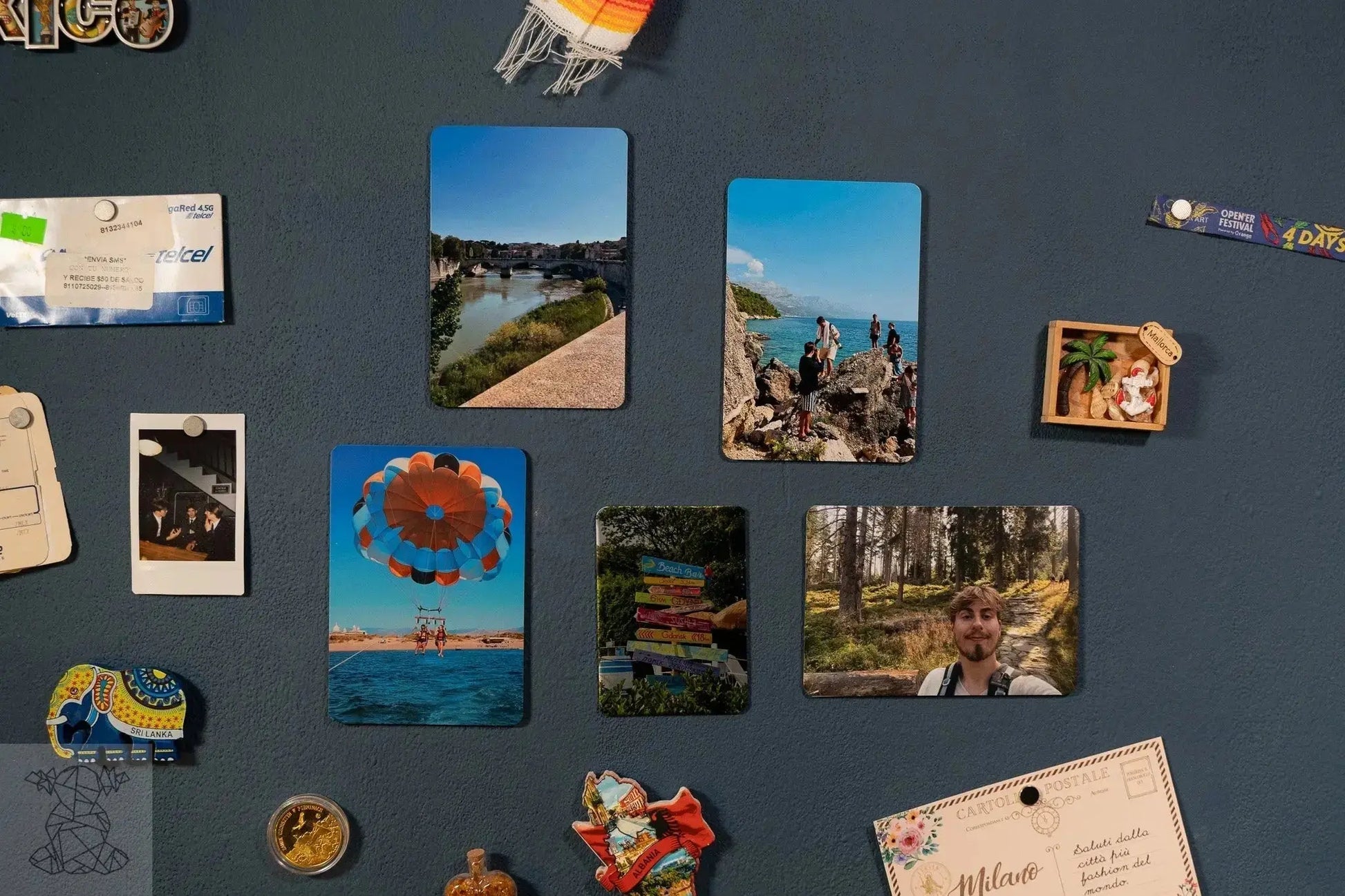 Gallery wall of multiple small glossy and matte metal travel prints on blue board, demonstrating magnetic collage display.