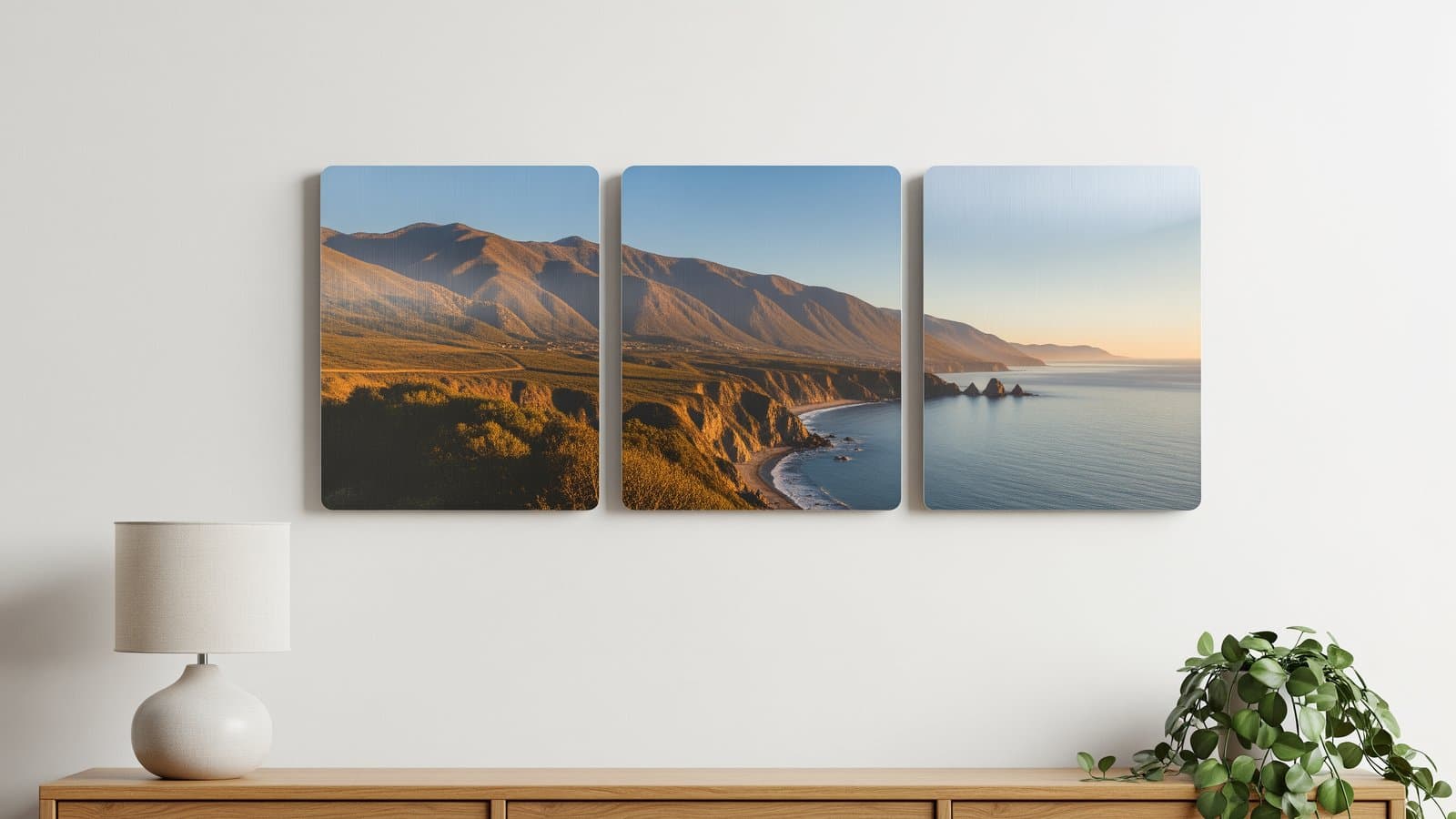 Een drieluik van drie bijpassende metaaldrukken opgehangen in een strakke rij boven een dressoir, één breed landschap verdeeld over de panelen