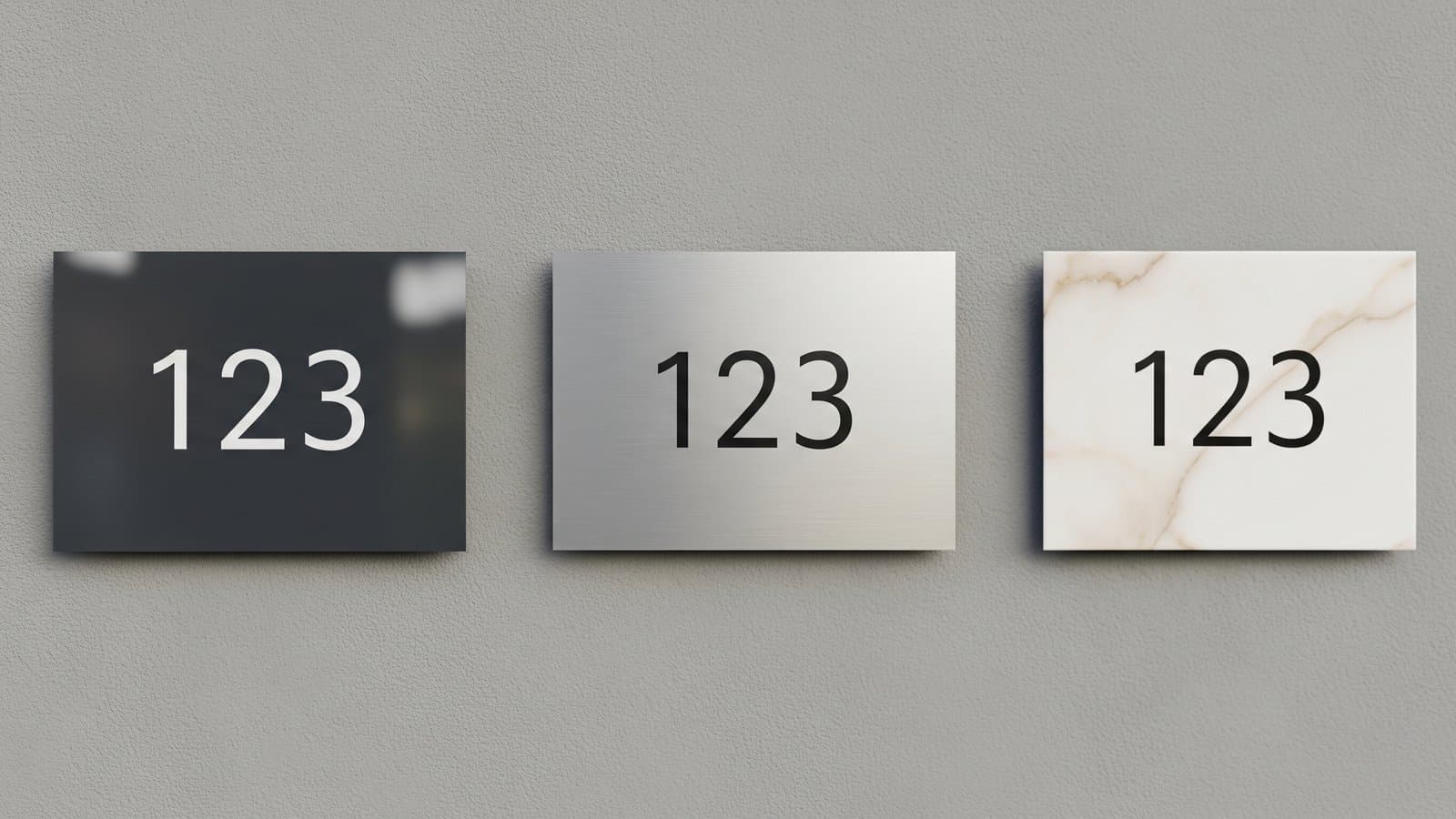 Tre targhe numero civico in materiali diversi montate fianco a fianco su una parete strutturata