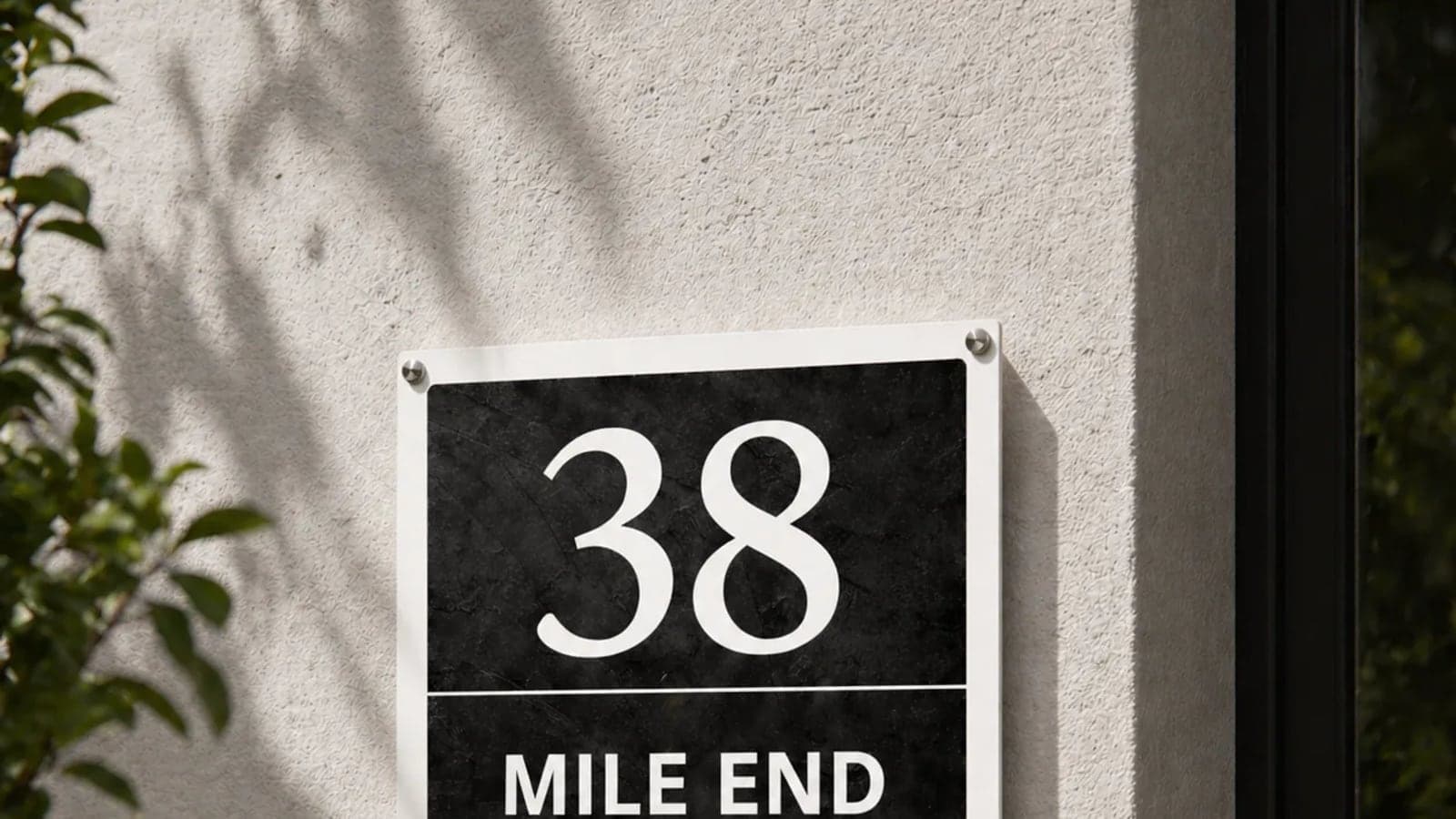 Modern minimalistisch huisnummerbord naast de voordeur, strakke typografie op een getextureerde muur
