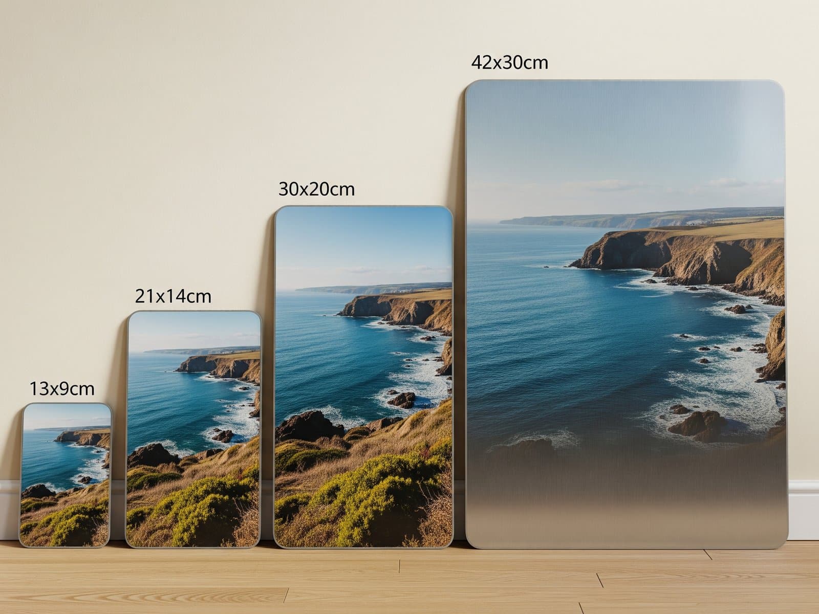Vier metalen fotoafdrukken in oplopende formaten tegen een wand, van een kleine bureauafdruk tot een grote wandafdruk
