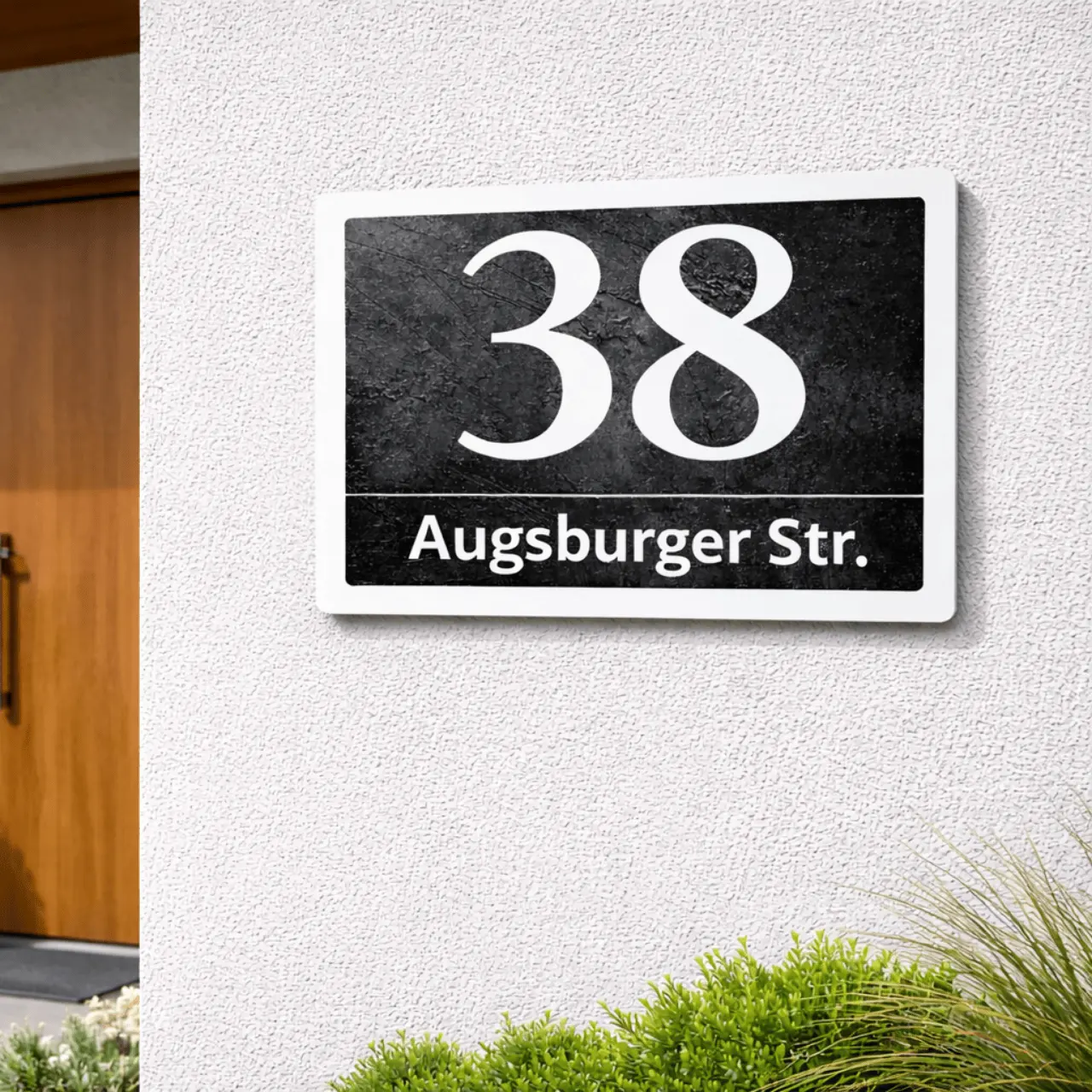 Raw-concrete anthracite metal address sign, number 38, flush adhesive-mounted on a white wall