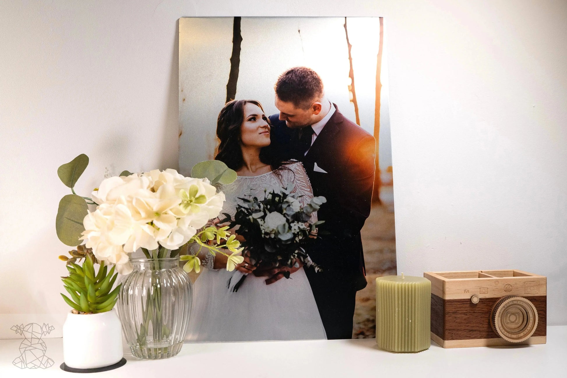 Large matte metal print of bride and groom on white shelf with vase, candle and wooden camera box, rich wedding colours.