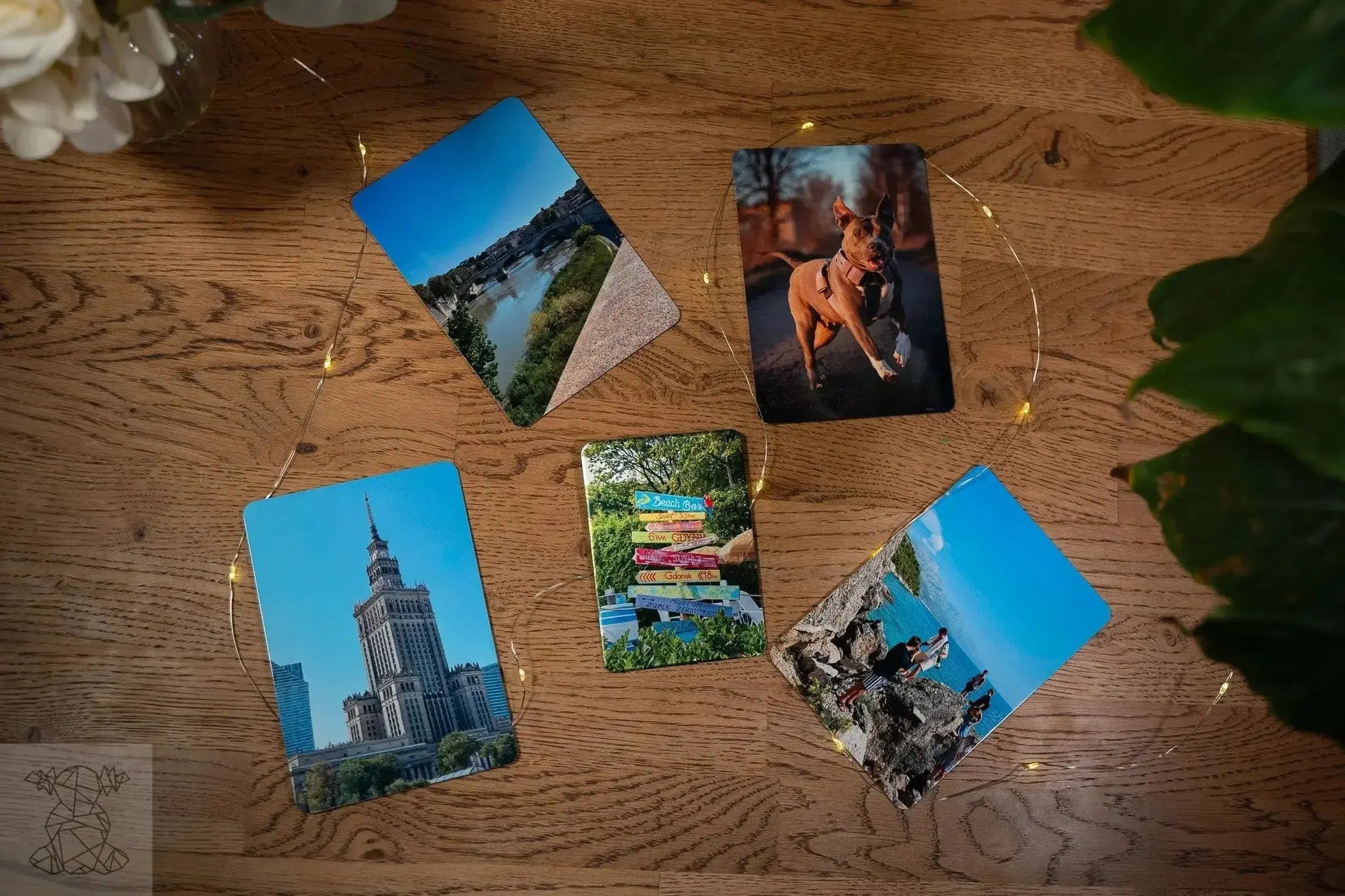 Five small glossy and matte metal photo prints arranged on wooden table with fairy lights, highlighting gift-size options.