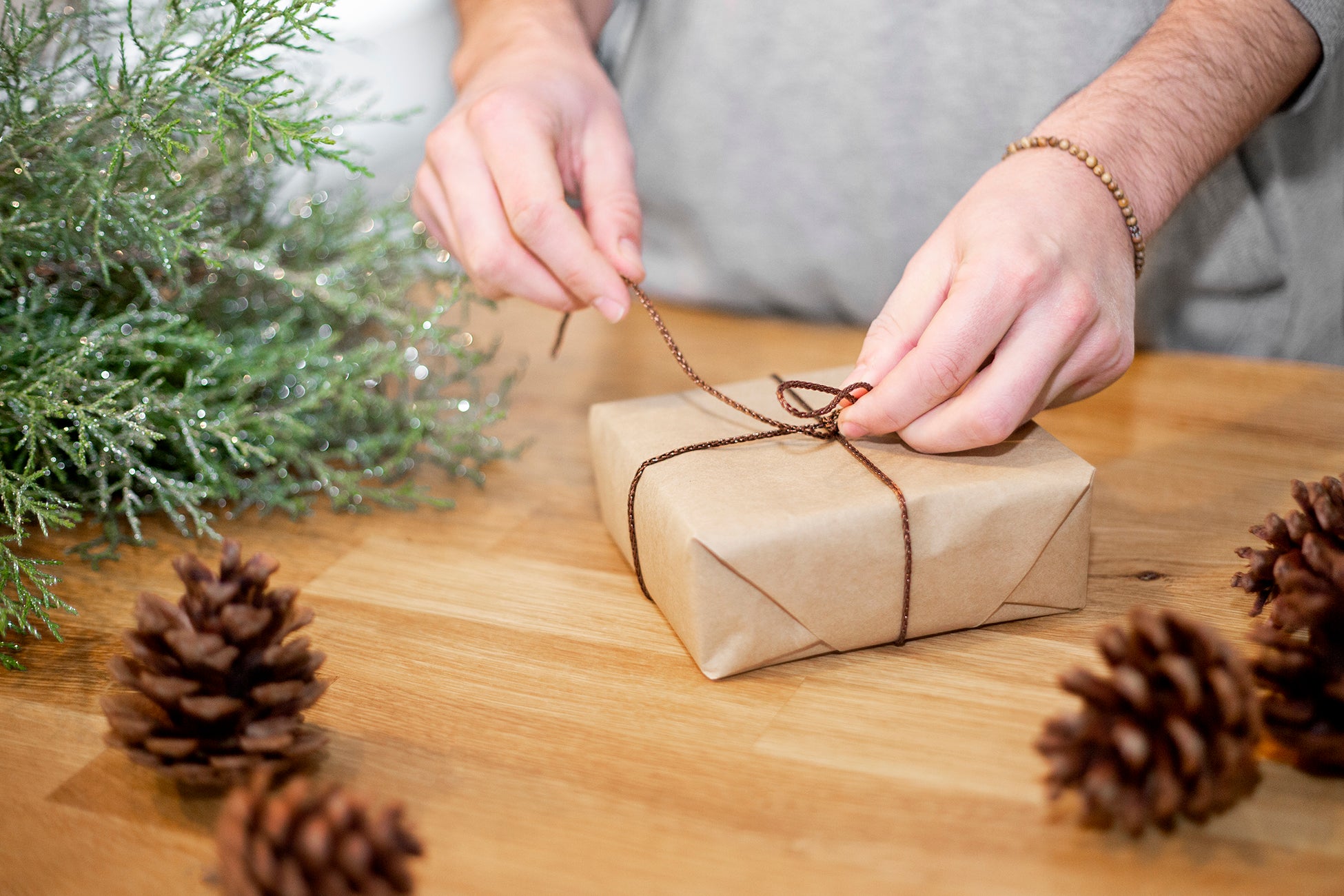 Hands wrapping a gift with twine on a wooden table, surrounded by pinecones — ideal for custom magnet gift sets or premium metal prints.