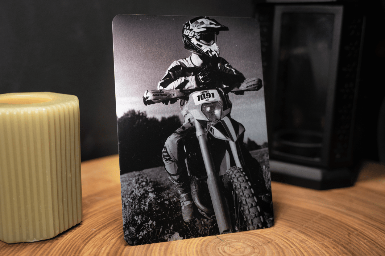 Small matte metal print of motocross rider in black-and-white beside candle and speaker, sharp detail.