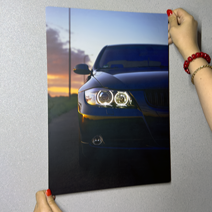 Person holding a poster of a black car against a gray wall
